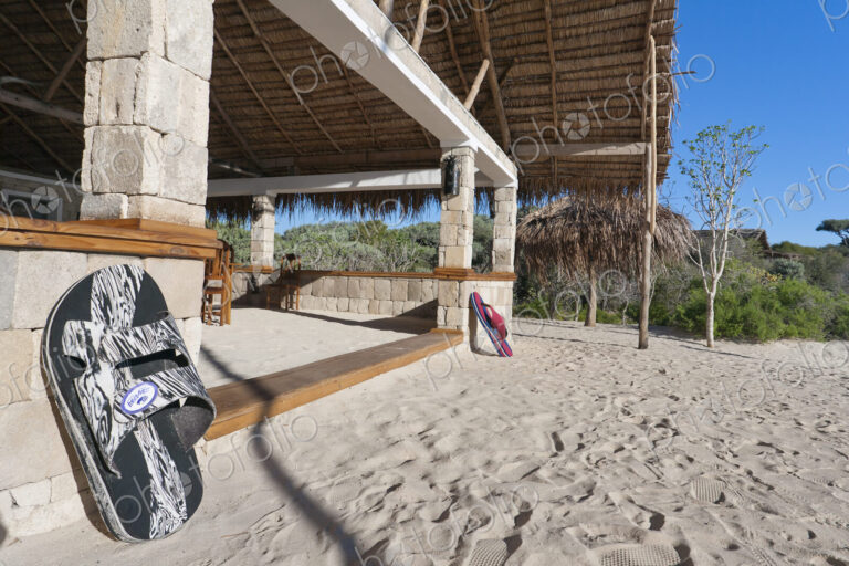 A beach resort building on a white sand beach, a pair of flipflops on the steps of a…