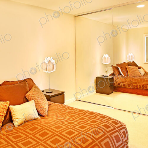 A bedroom with a large double bed and colourful bedding, and ceiling to floor mirrored…