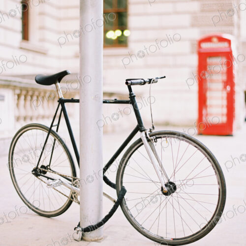 A bicycle chained and locked to a lamppost on a London street. A red public telephone… A bicycle chained and locked to a lamppost on a London street. A red public telephone…