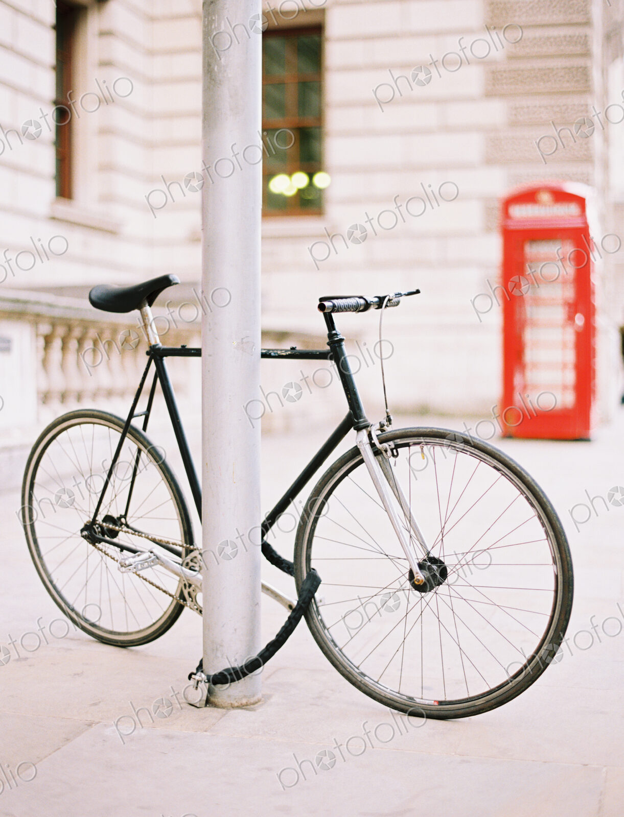 A bicycle chained and locked to a lamppost on a London street. A red public telephone…