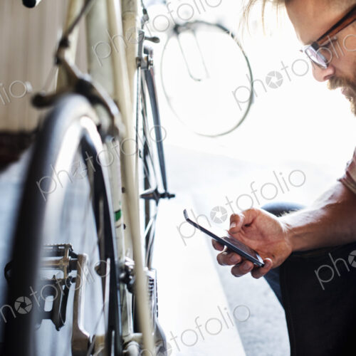A bike mechanic in a bicycle repair shop using a smart phone. A bike mechanic in a bicycle repair shop using a smart phone.