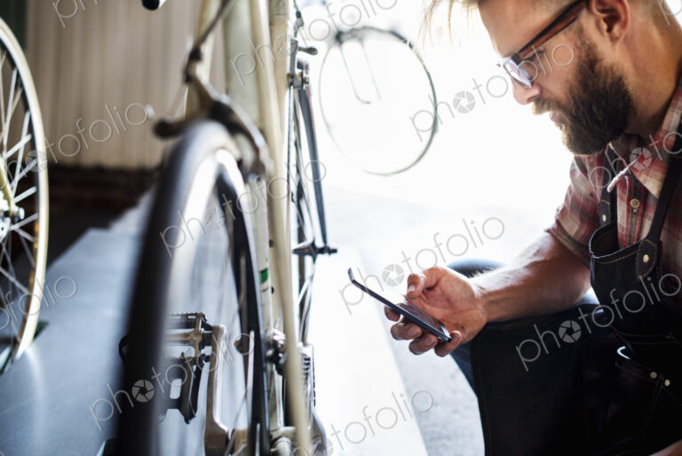 A bike mechanic in a bicycle repair shop using a smart phone.