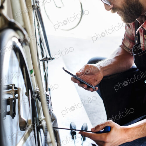 A bike mechanic in a bicycle repair shop using a smart phone. A bike mechanic in a bicycle repair shop using a smart phone.