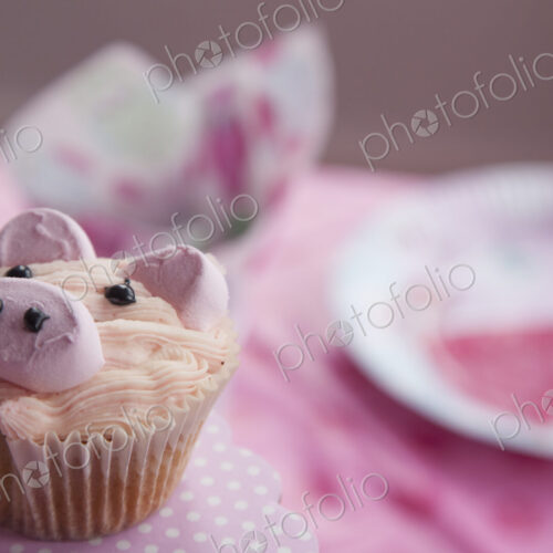 A birthday party table, with a pink cloth, and a cupcake decorated with the image of a…