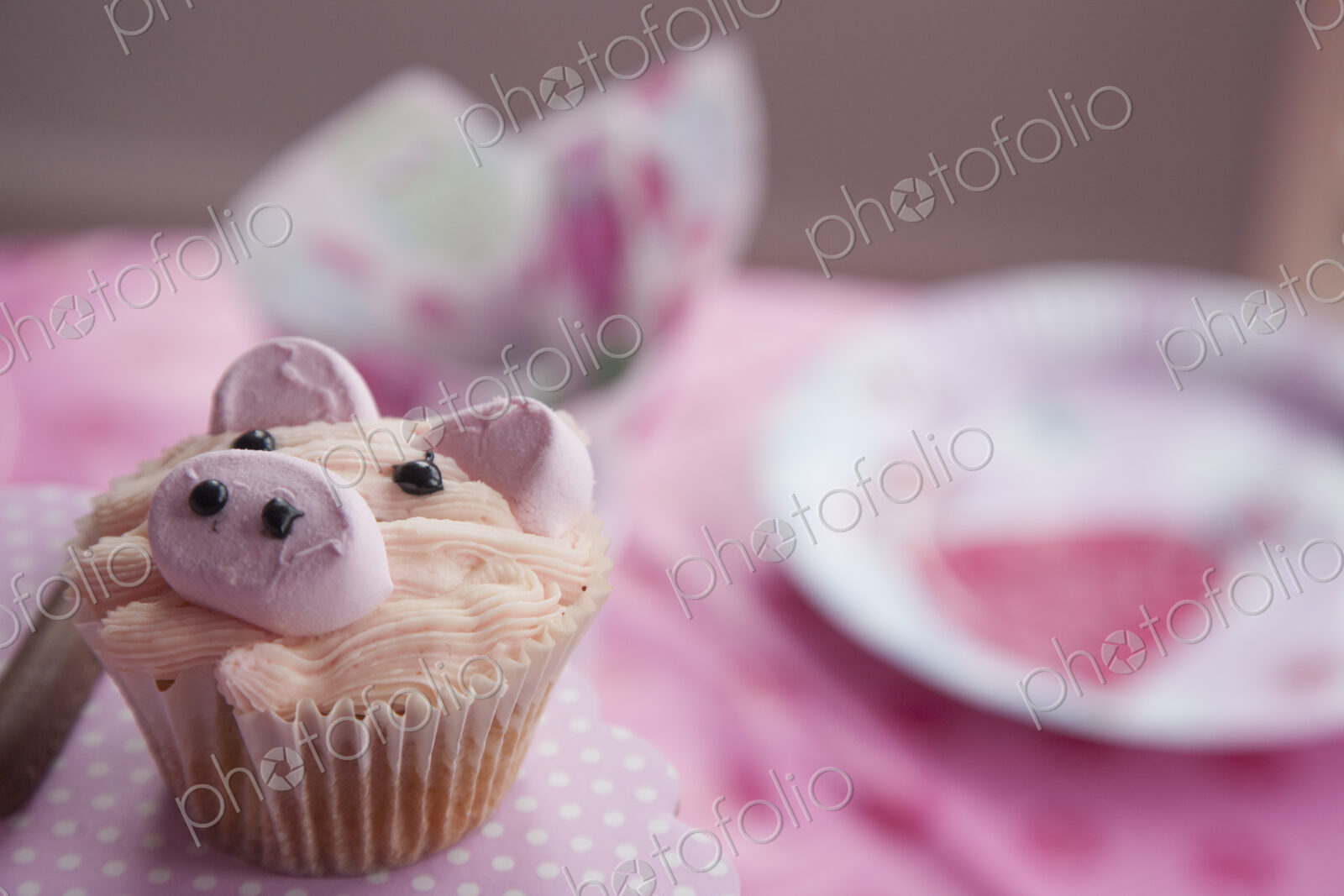 A birthday party table, with a pink cloth, and a cupcake decorated with the image of a…