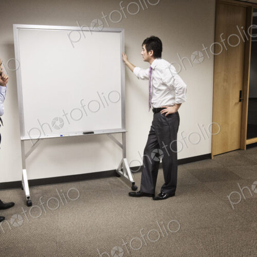 A black businessman and an asian businessman ponder the issue of an empty white board. A black businessman and an asian businessman ponder the issue of an empty white board.
