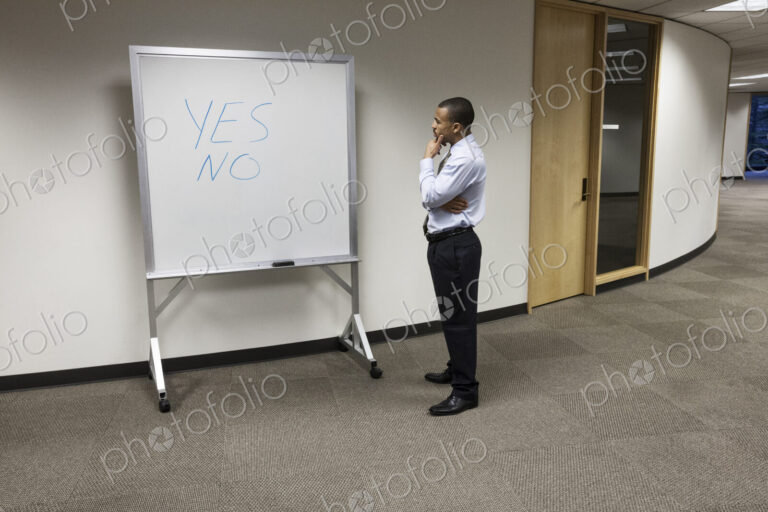 A black businessman musing by an office white board with the words Yes and No written…