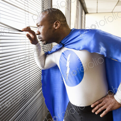 A black businessman office super hero looks out the window and checks his next…