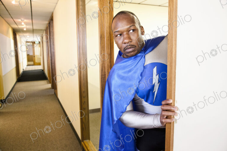 A black businessman office super hero peers out from his office into a hallway.