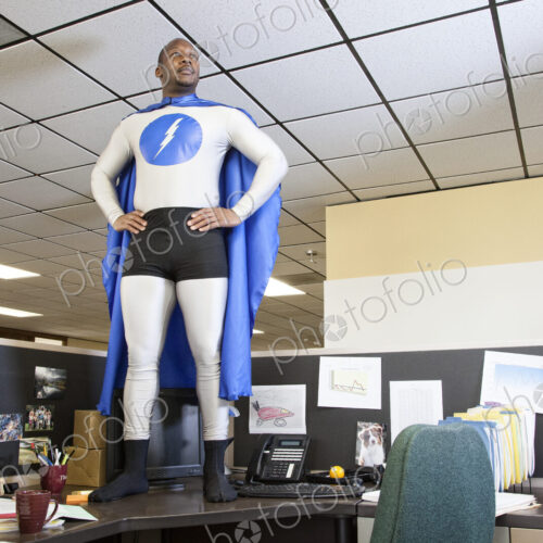 A black businessman office super hero stands on his cubicle desk ready for action. A black businessman office super hero stands on his cubicle desk ready for action.