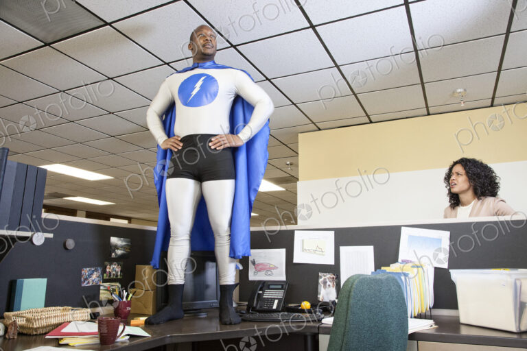 A black businessman office super hero stands on his cubicle desk ready for action.