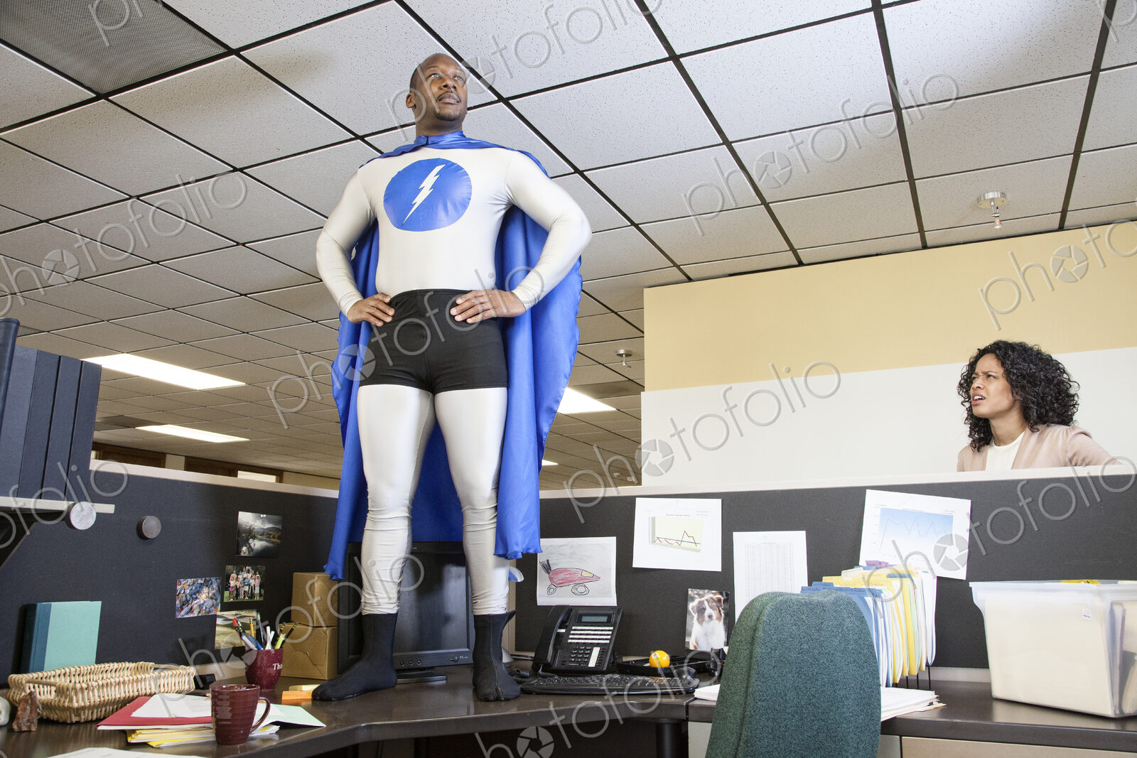 A black businessman office super hero stands on his cubicle desk ready for action.