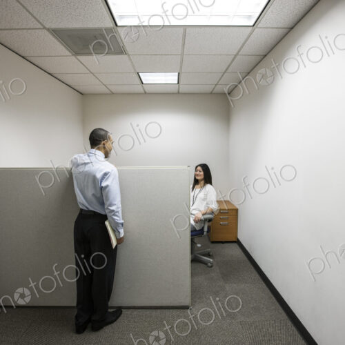 A black businessman talking to an asian businesswoman working in a small corner… A black businessman talking to an asian businesswoman working in a small corner…