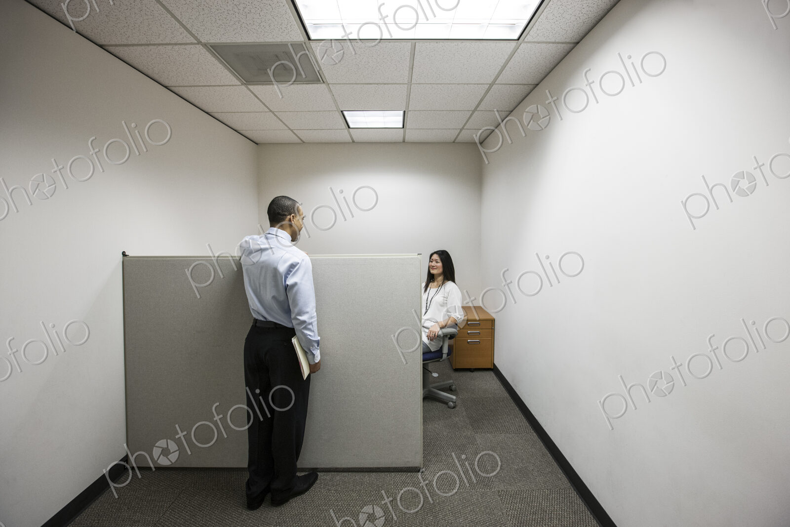 A black businessman talking to an asian businesswoman working in a small corner…