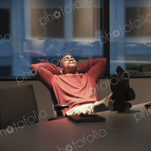 A black businessman with his feet up on a desk while working at night. A black businessman with his feet up on a desk while working at night.