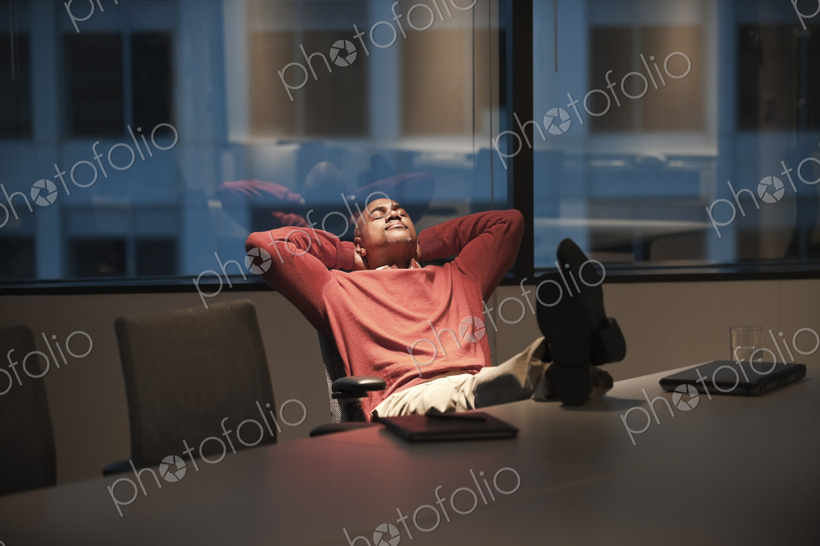 A black businessman with his feet up on a desk while working at night.