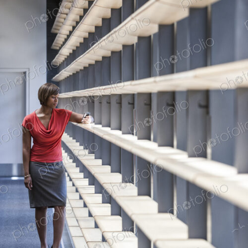 A black businesswoman checking her phone for a text in an office lobby. A black businesswoman checking her phone for a text in an office lobby.