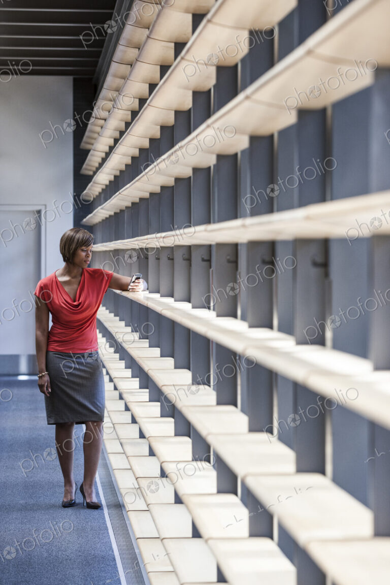A black businesswoman checking her phone for a text in an office lobby.