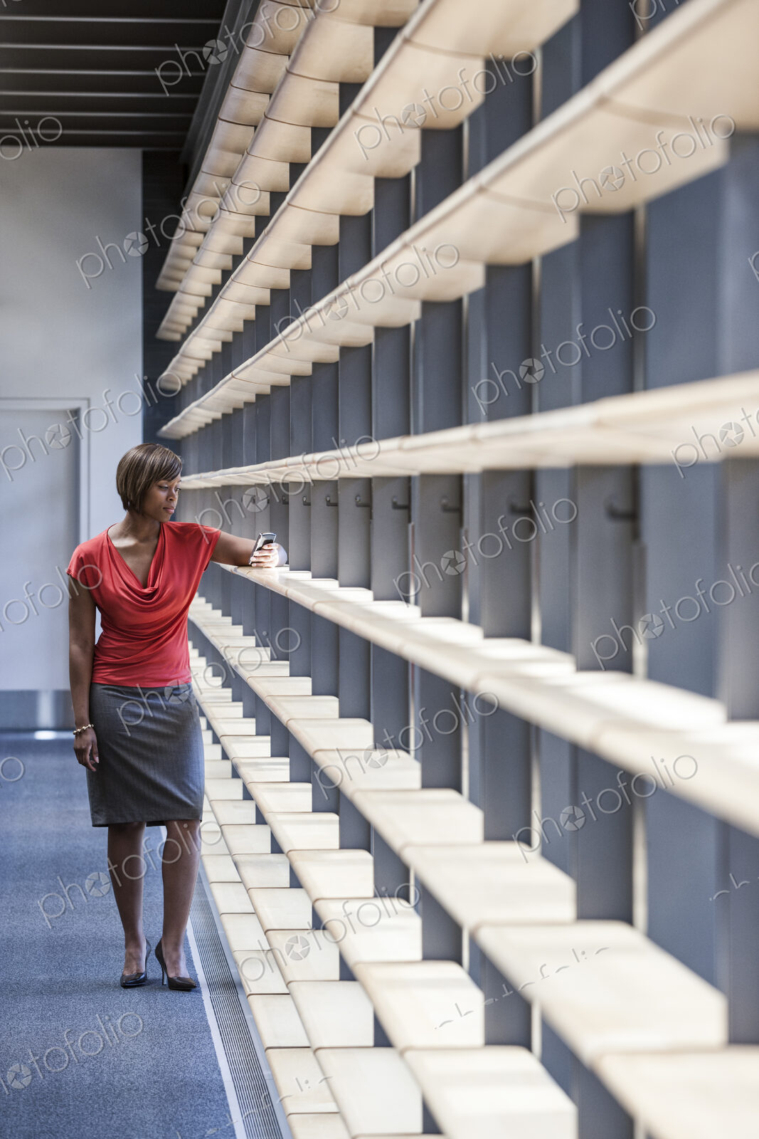 A black businesswoman checking her phone for a text in an office lobby.