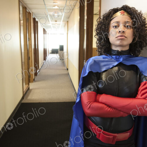 A black businesswoman office super hero standing in a hallway of her office.