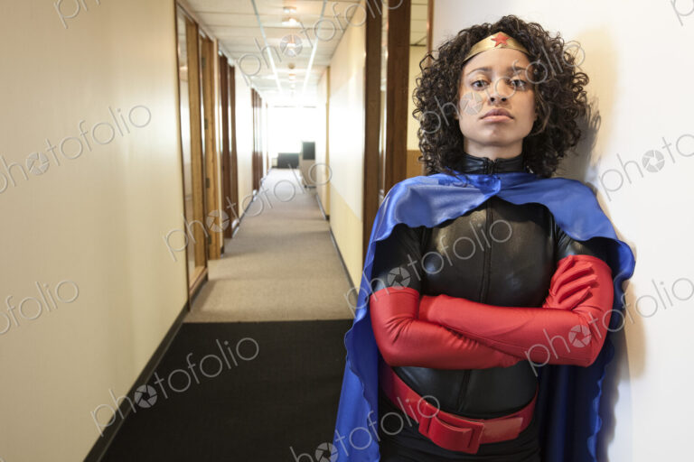 A black businesswoman office super hero standing in a hallway of her office.