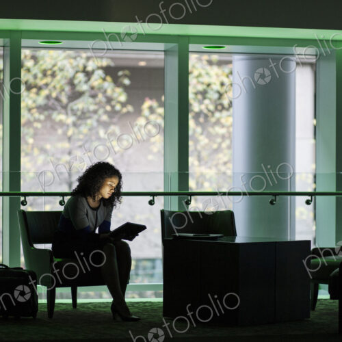 A black businesswoman sitting in front of windows in a darkened lobby area of a… A black businesswoman sitting in front of windows in a darkened lobby area of a…
