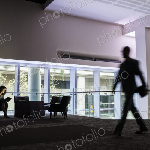 A black businesswoman sitting in front of windows in a darkened lobby area of a… A black businesswoman sitting in front of windows in a darkened lobby area of a…
