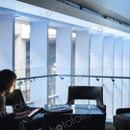 A black businesswoman sitting in front of windows in a darkened lobby area of a… A black businesswoman sitting in front of windows in a darkened lobby area of a…
