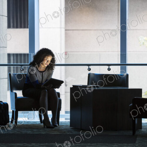 A black businesswoman sitting in front of windows in a darkened lobby area of a… A black businesswoman sitting in front of windows in a darkened lobby area of a…