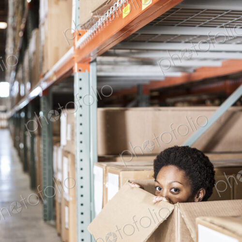 A black female worker hiding inside a cardboard box in a distribution warehouse.