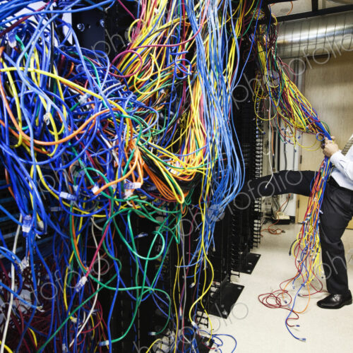 A black male techinician pulling on a tangled mess of CAT 5 cables in a computer…