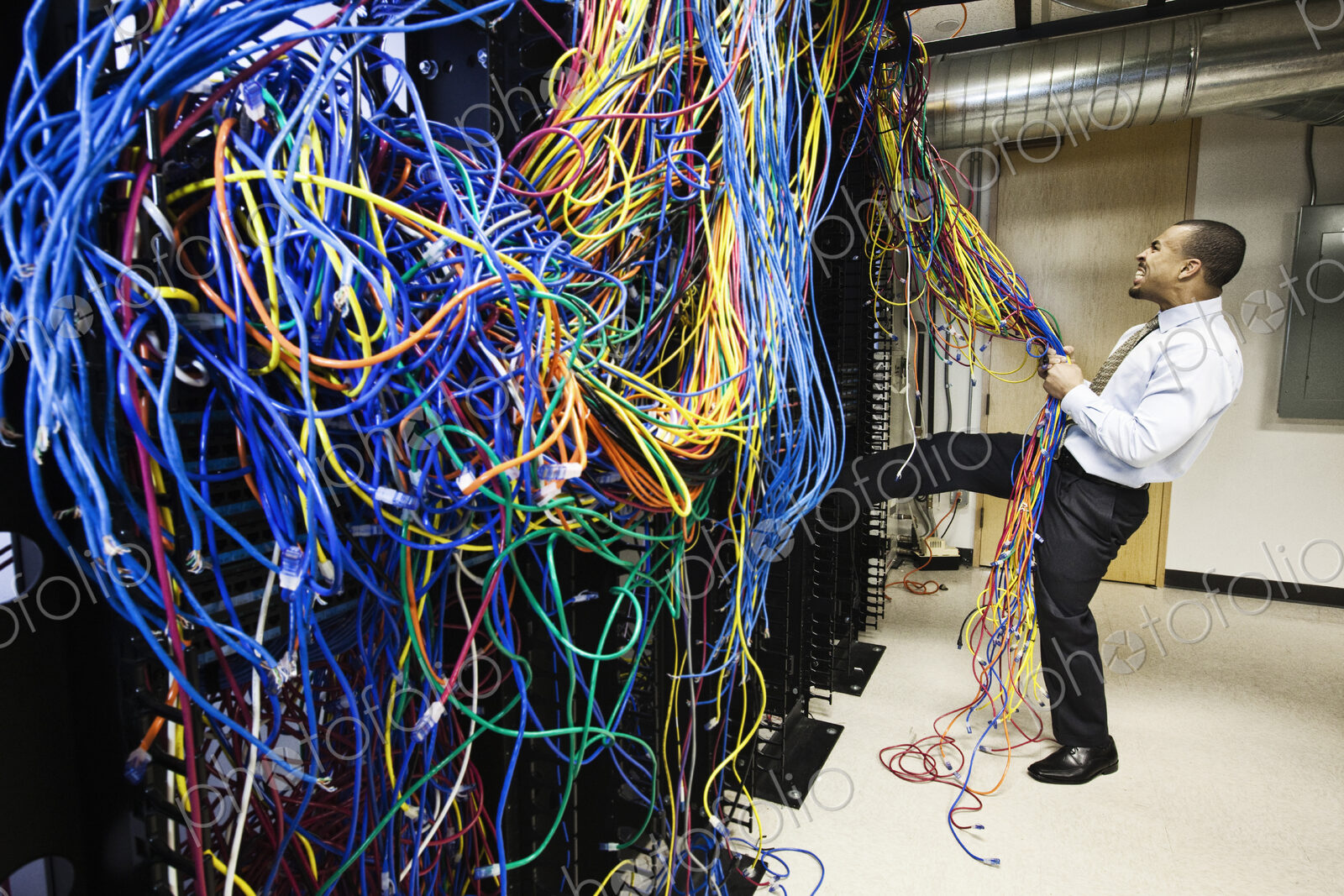 A black male techinician pulling on a tangled mess of CAT 5 cables in a computer…