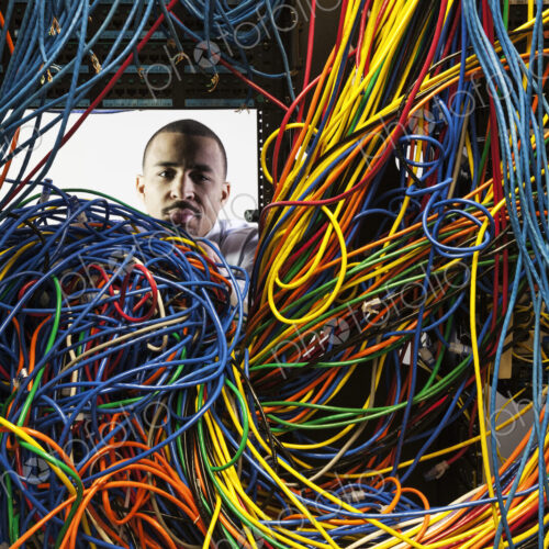 A black male technician woking on a tangled mess of CAT 5 cables in a server room.