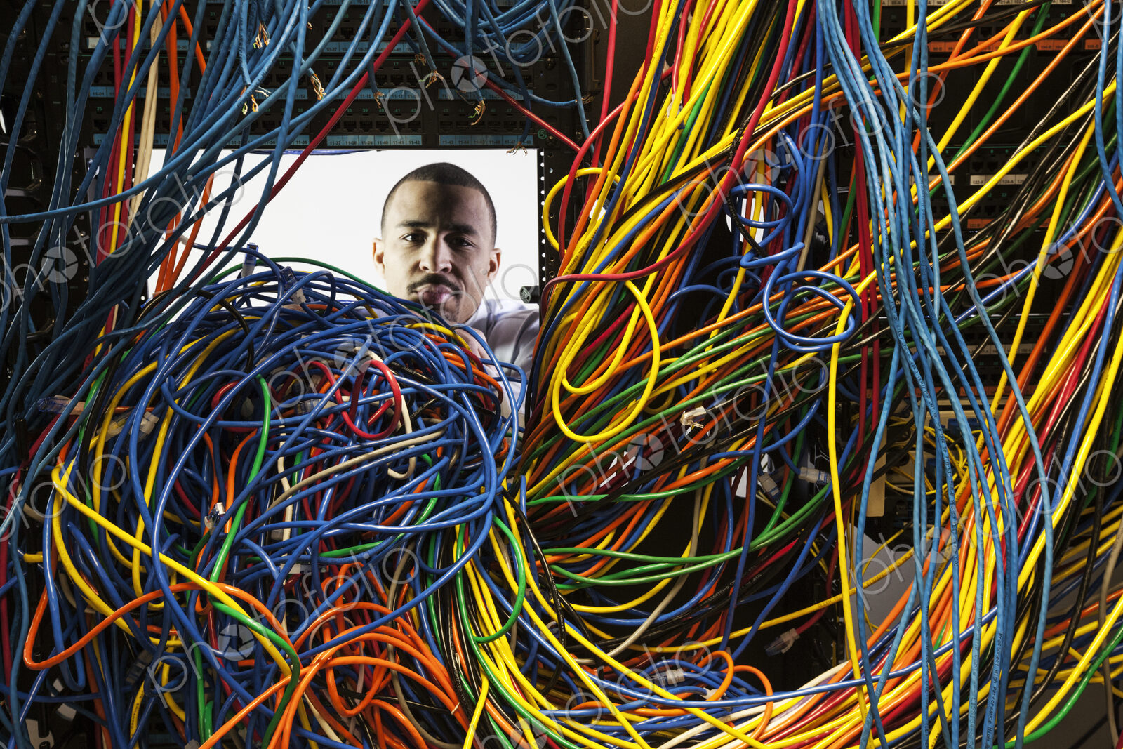 A black male technician woking on a tangled mess of CAT 5 cables in a server room.