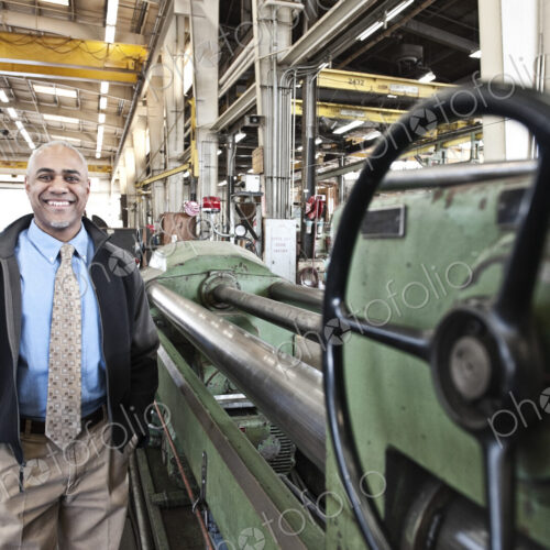 A black man owner of a sheet metal factory satnding on the floor of the factory.