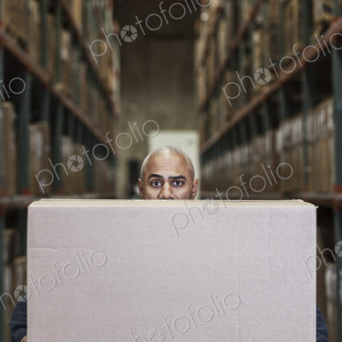 A black warehouse worker hidden behind a cardboard box in a distribution warehouse. A black warehouse worker hidden behind a cardboard box in a distribution warehouse.