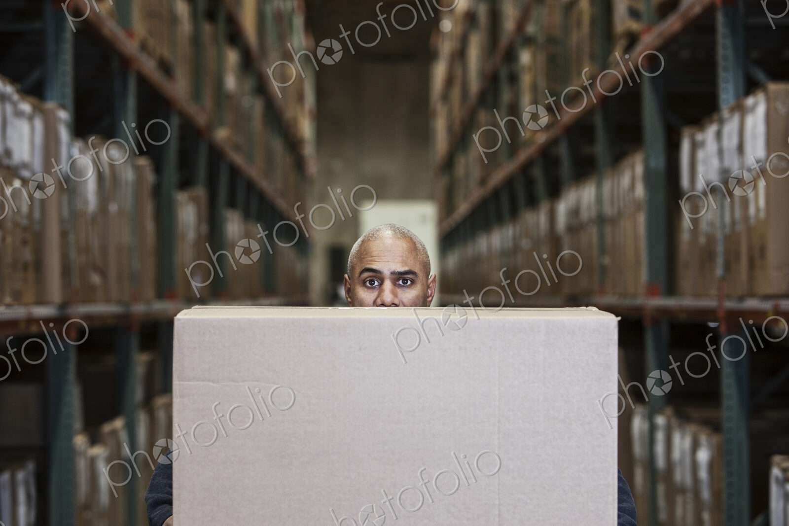 A black warehouse worker hidden behind a cardboard box in a distribution warehouse.