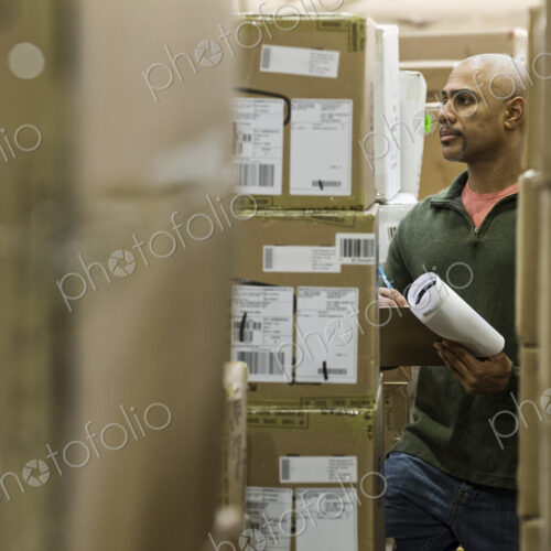 A black warehouse worker keeping track of boxed inventory in a distribution warehouse. A black warehouse worker keeping track of boxed inventory in a distribution warehouse.