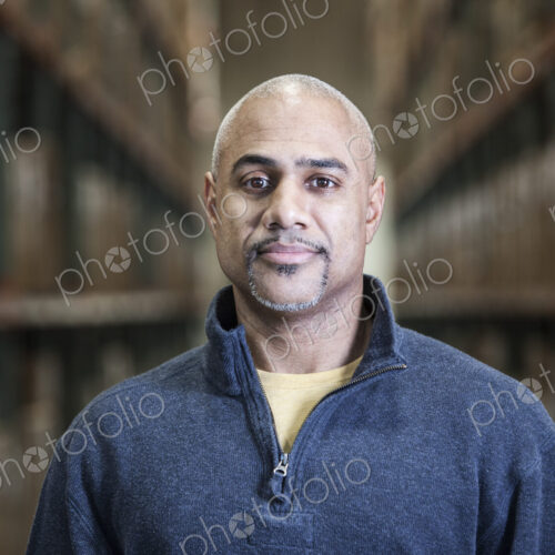 A black warehouse worker standing near boxed products in a distribution warehouse.