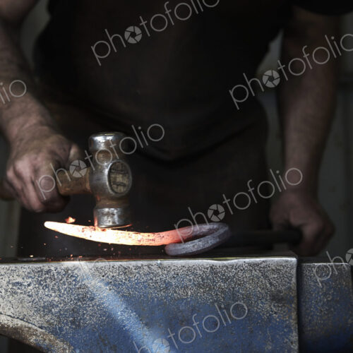 A blacksmith shaping a hot piece of iron on an anvil using a hammer. A blacksmith shaping a hot piece of iron on an anvil using a hammer.