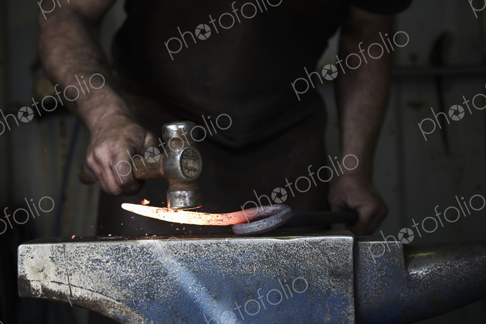 A blacksmith shaping a hot piece of iron on an anvil using a hammer.
