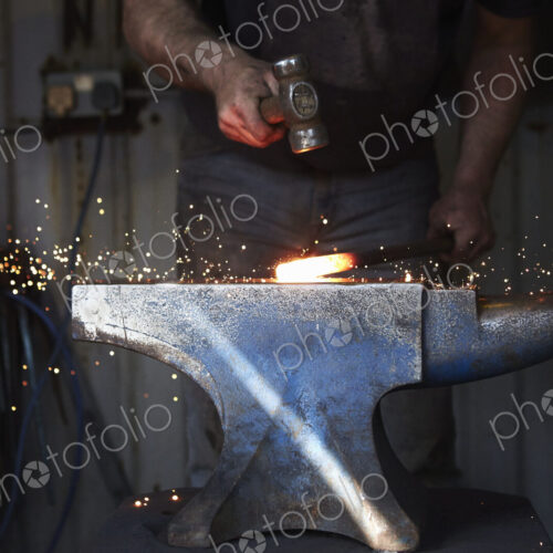 A blacksmith shaping a hot piece of iron on an anvil with a hammer, with sparks flying. A blacksmith shaping a hot piece of iron on an anvil with a hammer, with sparks flying.