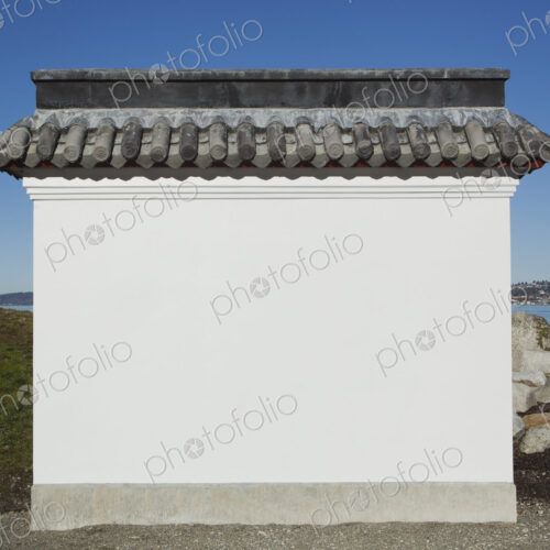 A blank wall painted white, with a layer of curved roof tiles, part of a pagoda or a…