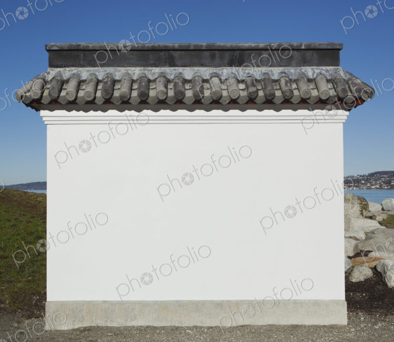 A blank wall painted white, with a layer of curved roof tiles, part of a pagoda or a…
