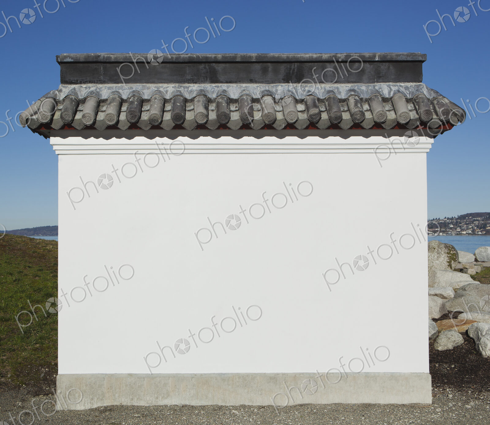 A blank wall painted white, with a layer of curved roof tiles, part of a pagoda or a…
