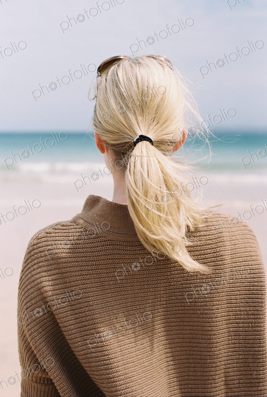 A blonde haired woman looking out to sea from the shore.