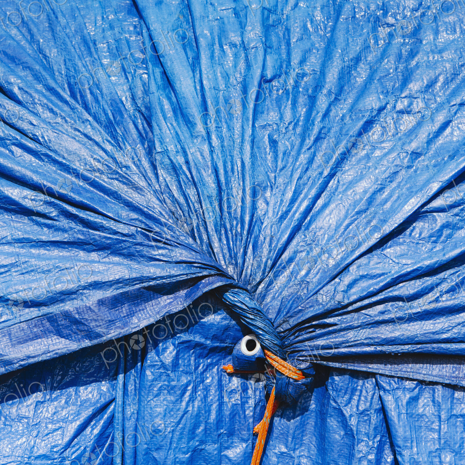 A blue tarpaulin, gathered and tied with rope as a covering over piles of commercial…