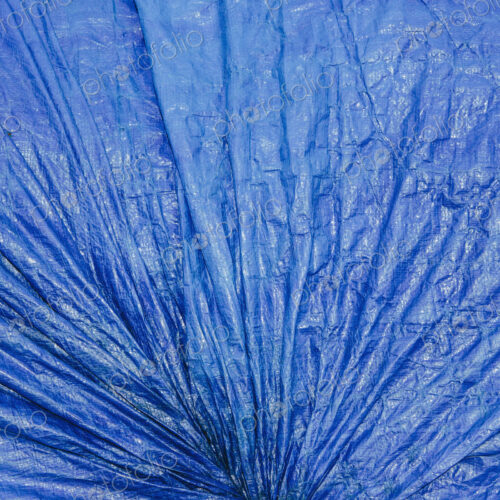 A blue tarpaulincovering gathered and tied as a covering over commercial fishing nets,…