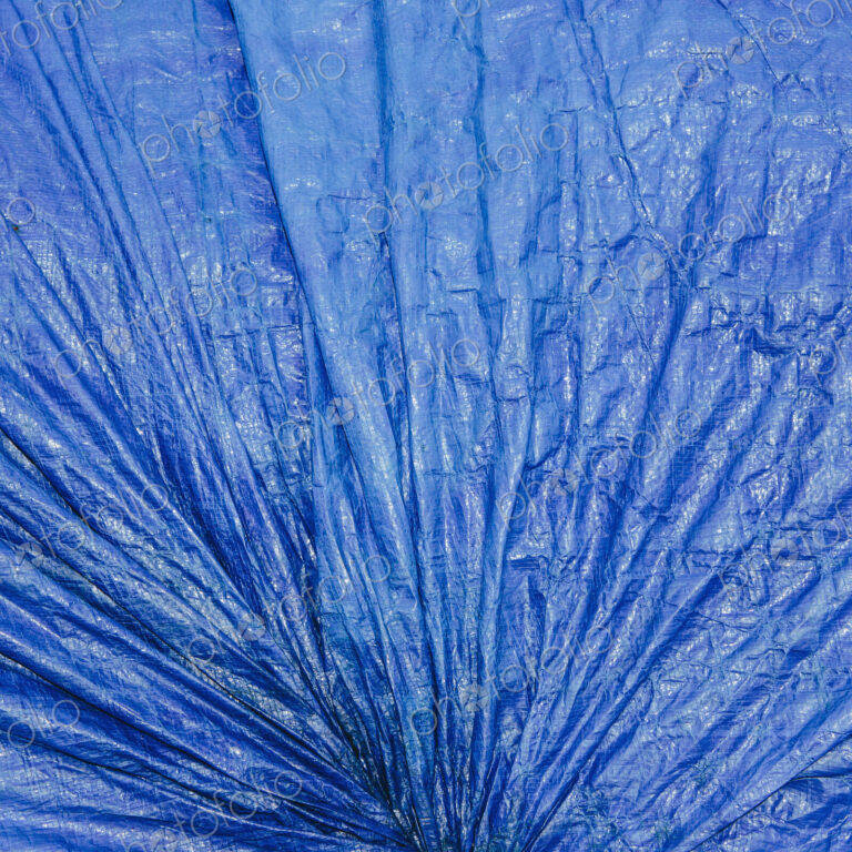 A blue tarpaulincovering gathered and tied as a covering over commercial fishing nets,…