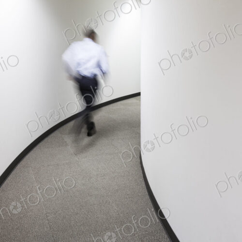 A blur of a businessman running in an office hallway. A blur of a businessman running in an office hallway.